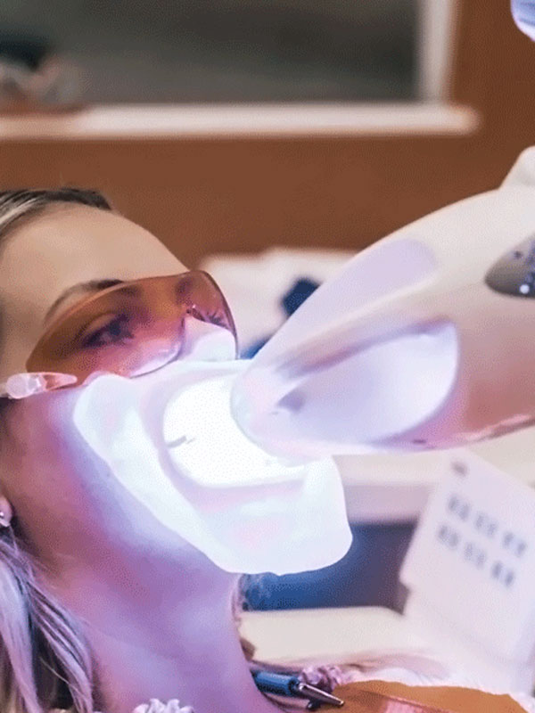 zahnaufhellung Dental professional wearing protective goggles uses a suction device near a patient in a dental chair with bright light.